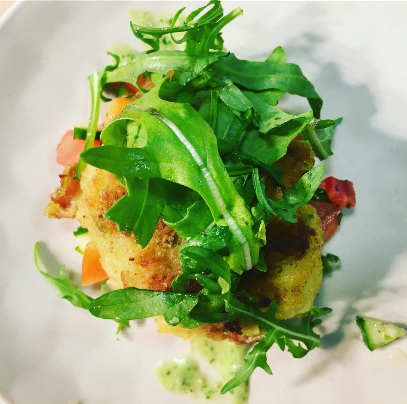 A golden fritter beneath a tall arugula salad